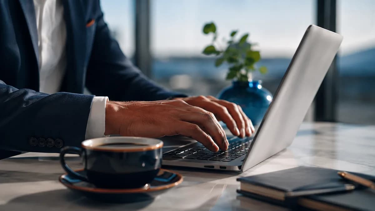 Manos sobre un teclado de ordenador con una taza de café, ilustrando la redacción de una plantilla de email de reembolso
